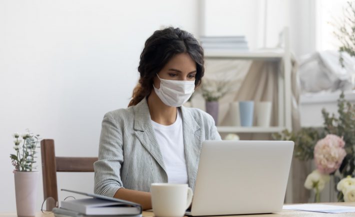 a woman with a face mask working on her laptop