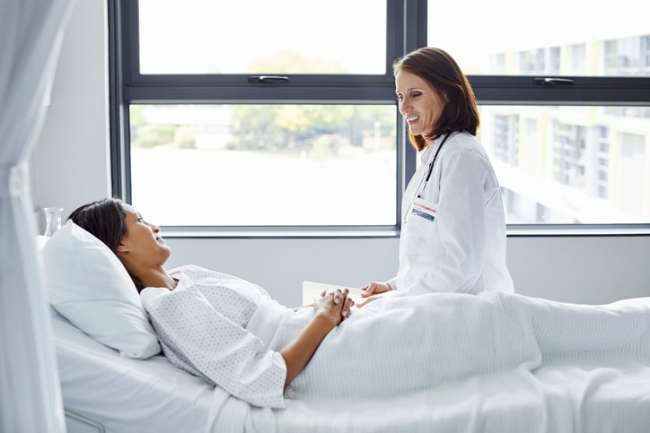 Smiling-doctor-looking-at-patient-lying-in-bed