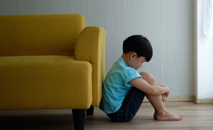 a sad boy leaning against the sofa