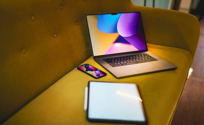 a laptop, phone, and tablet on a sofa