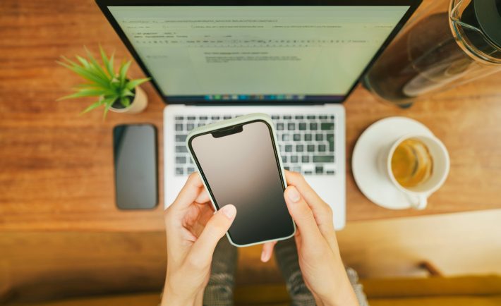 hands on a phone in front of a laptop