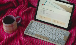 an ipad, keyboard, and cup on a red blanket